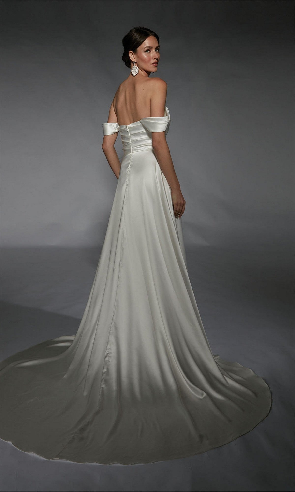A woman in the Alyce 7107 Long White Dress, featuring a satin A-line silhouette and long train, stands against a plain gray backdrop, looking over her shoulder.